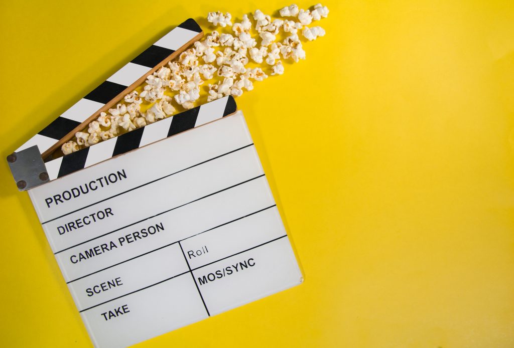 Movie clapboard and popcorn on yellow background