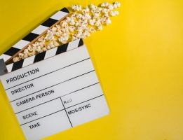 Movie clapboard and popcorn on yellow background