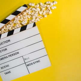 Movie clapboard and popcorn on yellow background