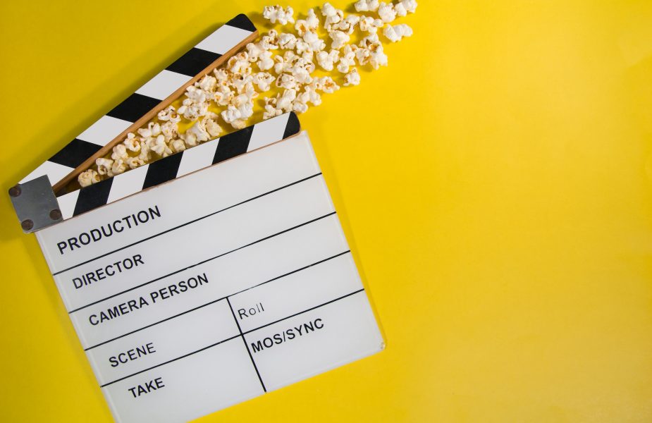 Movie clapboard and popcorn on yellow background