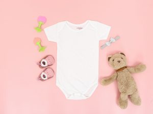 Baby shoes, onesie, rattle, and toy bear on pink background