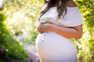 Pregnant woman in white dress holding stomach and standing outside