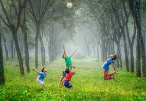 Four boys in forest jumping up trying to catch a soccer ball