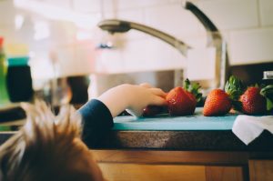Little boy reaching for strawberries by kitchen sink