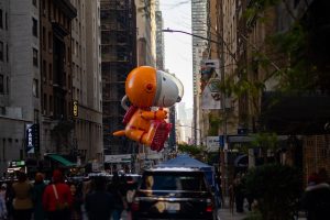 An orange and white Snoopy balloon floats over crowd in city