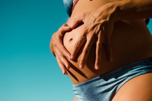 Closeup of woman in blue swimsuit holding pregnant stomach