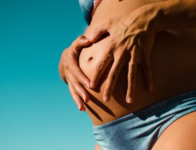 Closeup of woman in blue swimsuit holding pregnant stomach