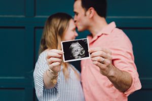 Man kissing woman's forehead holding a sonogram