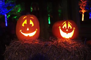 Two lit jack-o-lanterns with smiling faces on a hay bale