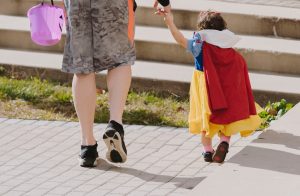 Little kid in Snow White costume holding dad's hand trick or treating