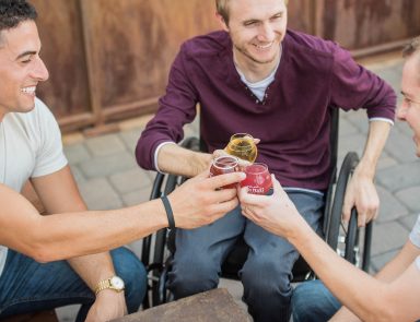 Three people, one in a wheel chair, cheers drinks