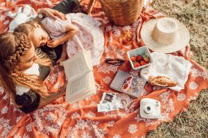 Mom and daughter on picnic blanket reading with strawberries and a polaroid camera