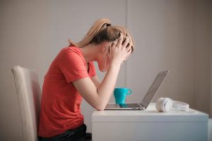 Person sitting at computer looking stressed out with head in their hands
