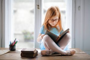 Little girl with glasses reading book