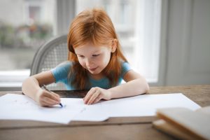 Little redhead girl ding homework at desk