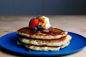Pancakes on a plate with fruit and syrup and butter