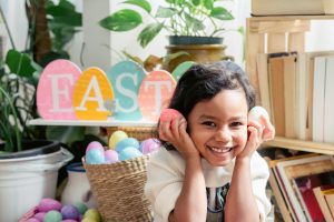 Little girl smiling in front of Easter sign holding eggs