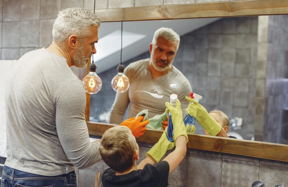 Child cleaning mirror with help from dad