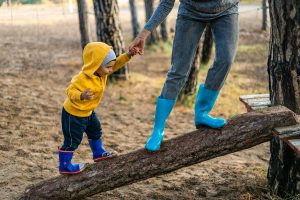 Little boy in rain coat and rain boots holding his parent's hand