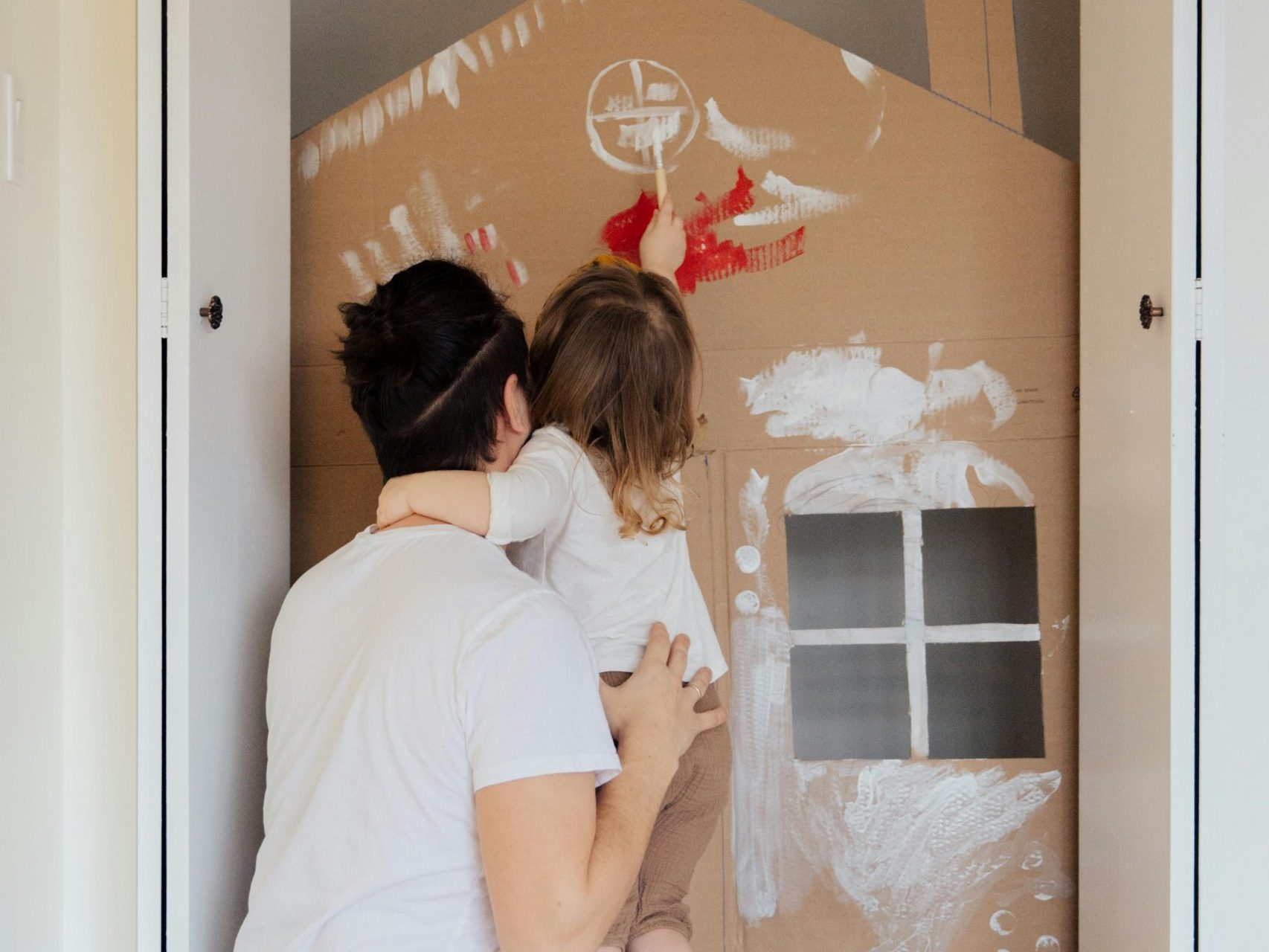 Father helping child paint a play house