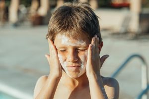 Kid rubbing sunblock on his face